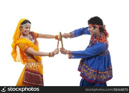 Side view of happy couple performing Dandiya Raas against white background