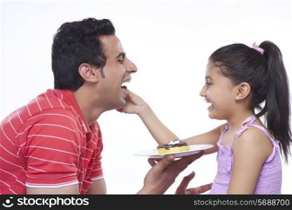 Side view of happy daughter feeding donut to father over white background