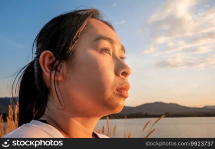 Side view of happy hopeful woman looking away to nature reflection on water at sunset lakeside.