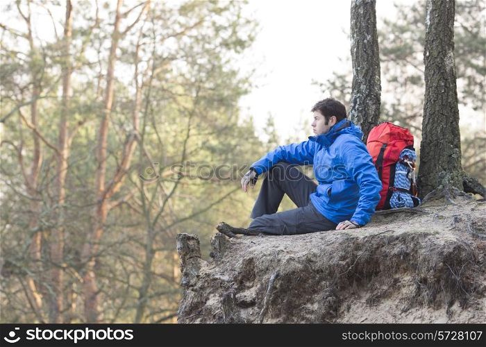 Side view of hiker sitting on edge of cliff in forest