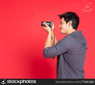 Side view of hipster in casual fashion shirt taking photo with dslr camera. half body portrait isolated on red studio background.