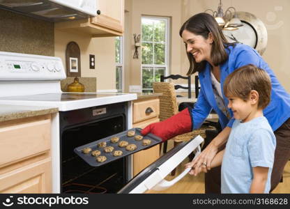 Side view of Hispanic mother and son putting cookies into oven.