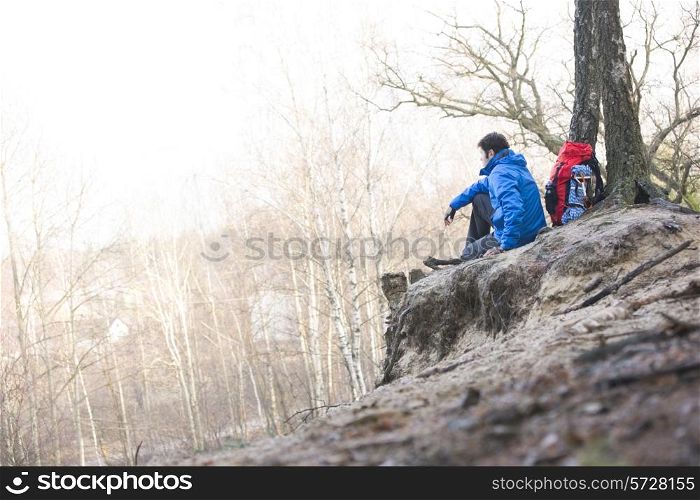Side view of male hiker sitting on edge of cliff in forest