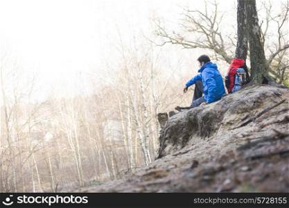 Side view of male hiker sitting on edge of cliff in forest