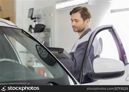 Side view of male maintenance engineer holding tablet PC while examining car in workshop