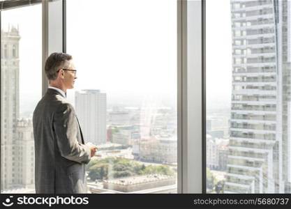 Side view of mature businessman looking through office window