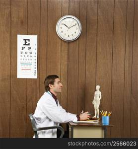 Side view of mid-adult Caucasian male doctor sitting at desk.