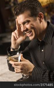 Side view of mid adult Caucasian man holding martini with hand to head smiling.