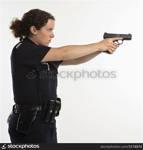 Side view of mid adult Caucasian policewoman standing and aiming handgun with arms outstretched.