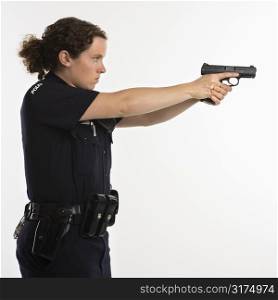 Side view of mid adult Caucasian policewoman standing and aiming handgun with arms outstretched.
