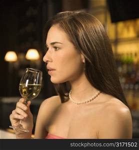 Side view of mid adult Caucasian woman sitting at bar drinking glass of white wine.