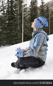 Side view of mid adult Caucasian woman wearing blue ski clothing sitting in snow in lotus position.