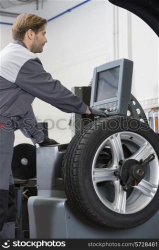 Side view of mid adult male mechanic repairing car&rsquo;s wheel in workshop