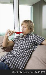 Side view of mid-adult man drinking wine in living room at home