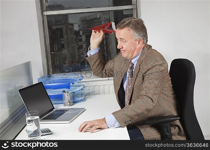 Side view of middle-aged businessman throwing paper airplane in office