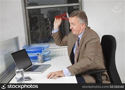 Side view of middle-aged businessman throwing paper airplane in office