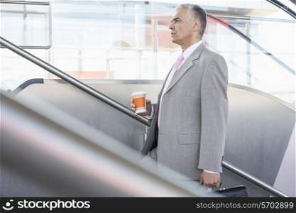 Side view of middle aged businessman with coffee cup walking up stairs in railroad station