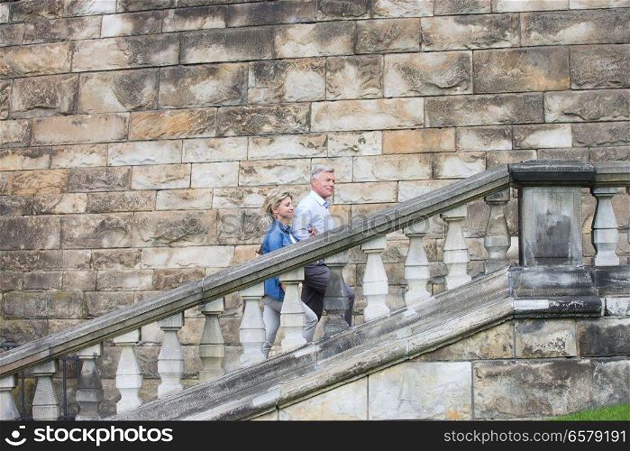Side view of middle-aged couple climbing steps outside old building