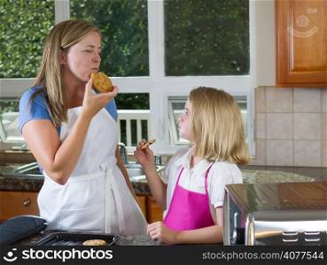 Side view of mother, eyes closed, eating her freshly baked cookie with her young daughter watching her enjoy the moment