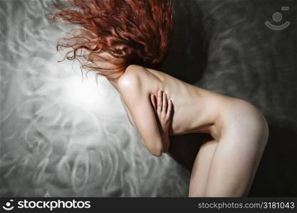 Side view of nude Caucasian woman flipping long hair in air.