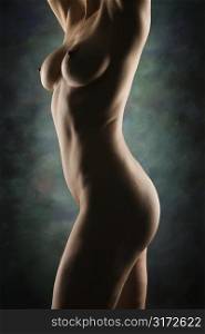 Side view of nude Caucasian woman standing with arms raised.
