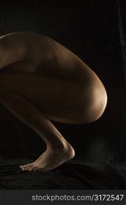 Side view of nude Hispanic mid adult woman crouching with knees to chest.