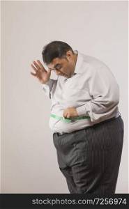 Side view of obese man measuring his stomach with measuring tape and feeling shocked