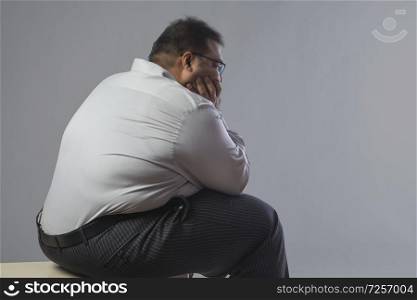 Side view of obese man sitting in sad mood with chin resting on hand