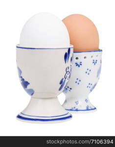 side view of pair of boiled eggs in ceramic egg cups isolated on white background, the white egg on foreground