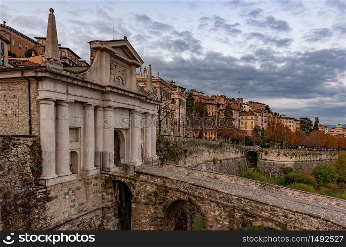 Side view of Porta San Giacomo and the walls of the upper city of Bergamo. Fortified and historical urban complex in Italy. Cityscape with cloudy sky.