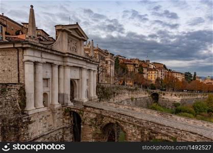 Side view of Porta San Giacomo and the walls of the upper city of Bergamo. Fortified and historical urban complex in Italy. Cityscape with cloudy sky.