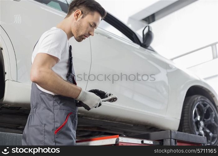 Side view of repairman holding tool while standing by car in workshop