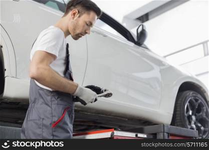 Side view of repairman holding tool while standing by car in workshop