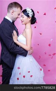 Side view of romantic wedding couple embracing against pink background