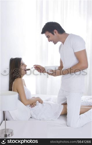 Side view of romantic young man feeding woman in bed