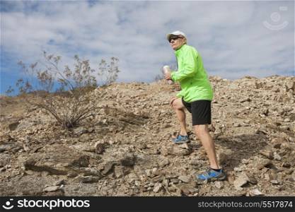 Side view of senior man holding water bottle while standing on mountain