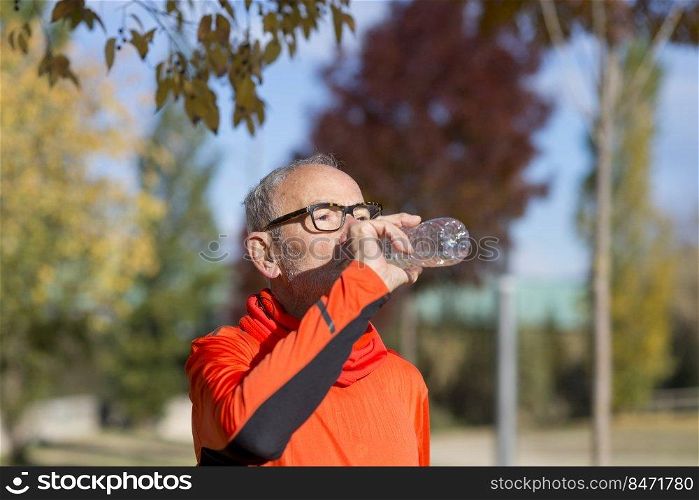 Side view of senior man resting and drinking water after workout while looking away