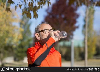 Side view of senior man resting and drinking water after workout while looking away