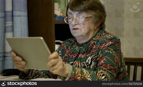 Side view of senior woman scrolling photos on the tablet computer and telling something