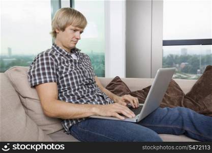 Side view of serious mid-adult man using laptop on sofa at home