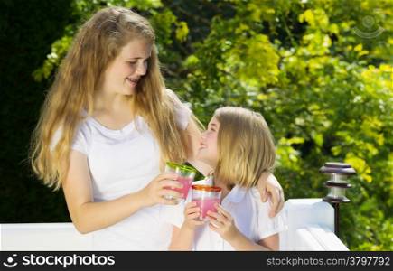 Side view of sisters hugging each other while drinking cold lemonade outdoors on patio