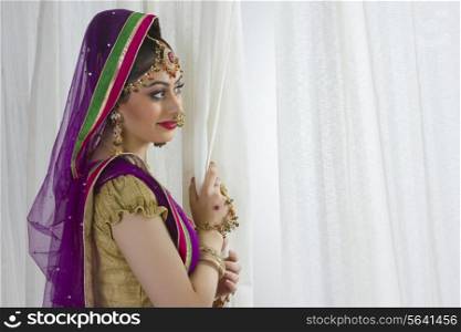 Side view of smiling bride standing by window at home