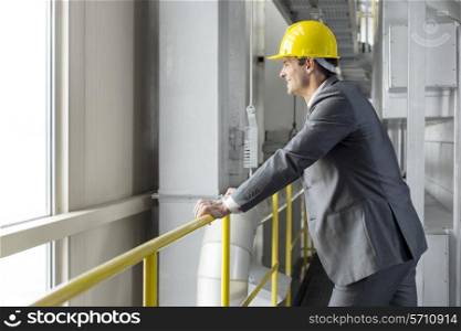 Side view of smiling male architect leaning on railing in industry