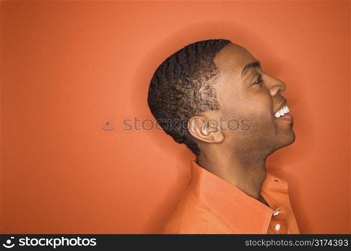 Side view of smiling young African-American man on orange background.