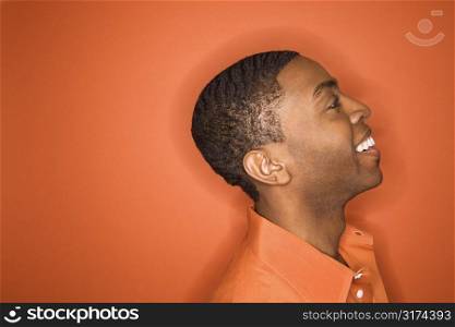 Side view of smiling young African-American man on orange background.