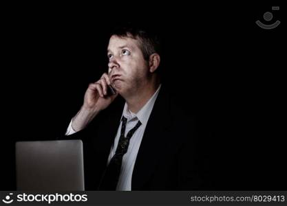Side view of stressed business man on cell phone while working. Dark background with light on face.