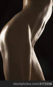 Side view of thighs and stomach of nude Hispanic mid adult woman glistening with body oil.
