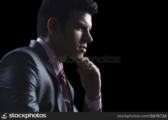 Side view of thoughtful businessman with hand on chin against black background