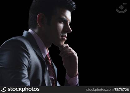 Side view of thoughtful businessman with hand on chin against black background