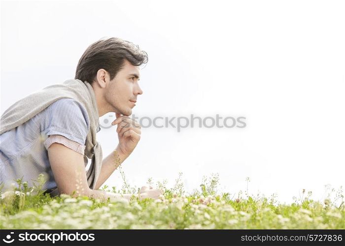 Side view of thoughtful young man lying on grass against clear sky
